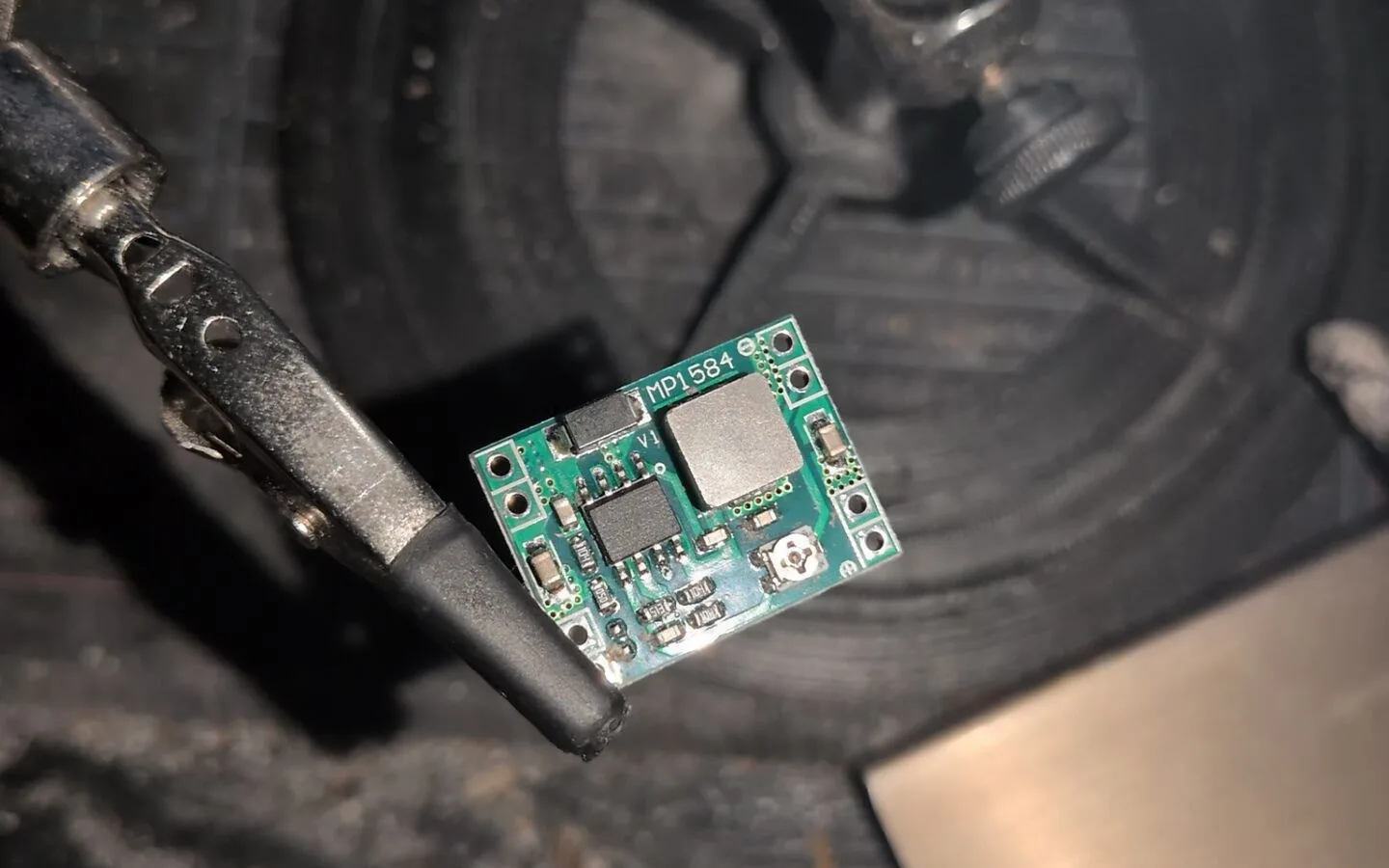 Live stream in a web browser: a close-up of a small green MP1584 power module held in a helping-hands clamp